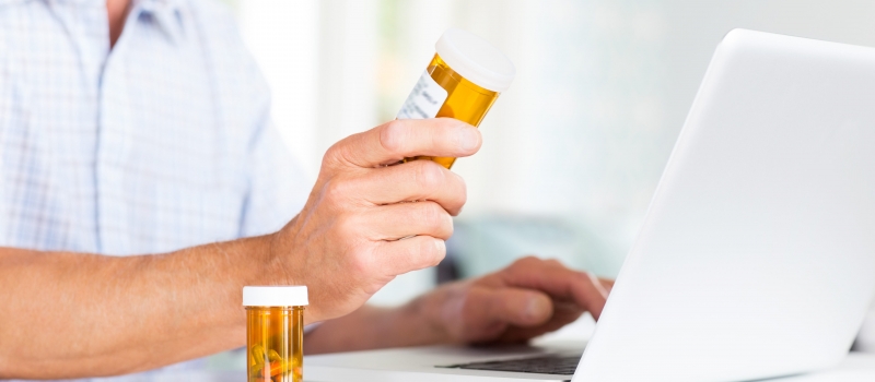 Senior Man With Pill Bottles Using Laptop At Table. Senior Man With Pill Bottles Using Laptop At Table.